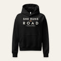 She Runs the Road Hoodie in Black, front view, SHE RUNS THE ROAD chest lettering, on a cream background