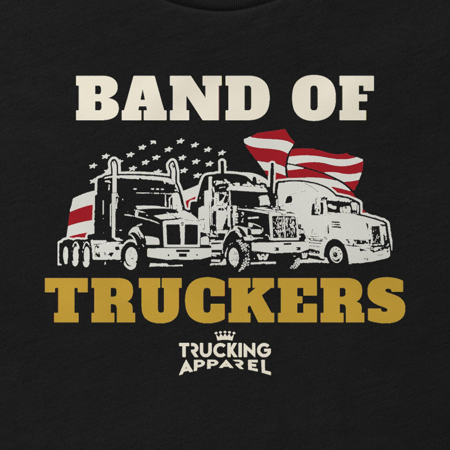 Band of Truckers Tee, close-up of BAND OF TRUCKERS around three big rigs in front of a waving American flag and a field of stars, with the Trucking Apparel crown logo underneath.