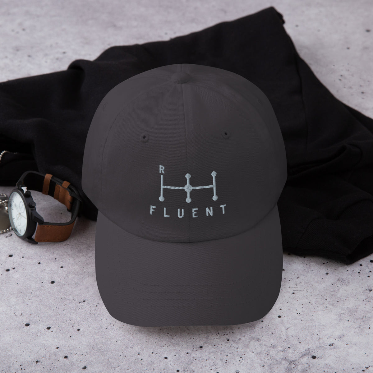 Fluent Dad Cap in dark grey, front view laid on a dark shirt with a wristwatch.