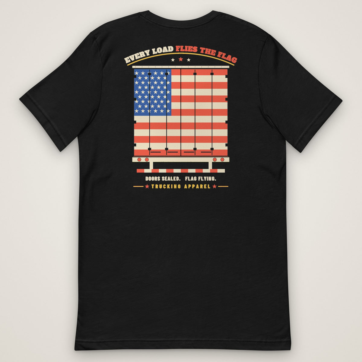Every Load Flies the Flag Tee in black, back view laid flat showing the EVERY LOAD FLIES THE FLAG back print: an American flag across a trailer's rear swing doors, with DOORS SEALED. FLAG FLYING. and the Trucking Apparel signature.