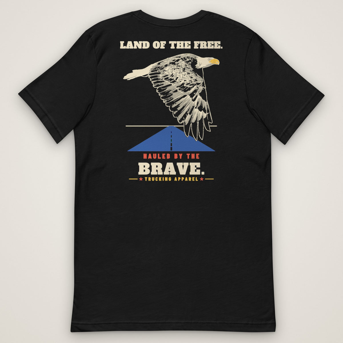 Land of the Free. Hauled by the Brave. Tee in black, back view laid flat showing the LAND OF THE FREE. HAULED BY THE BRAVE. back print: an engraving-style eagle over a highway.