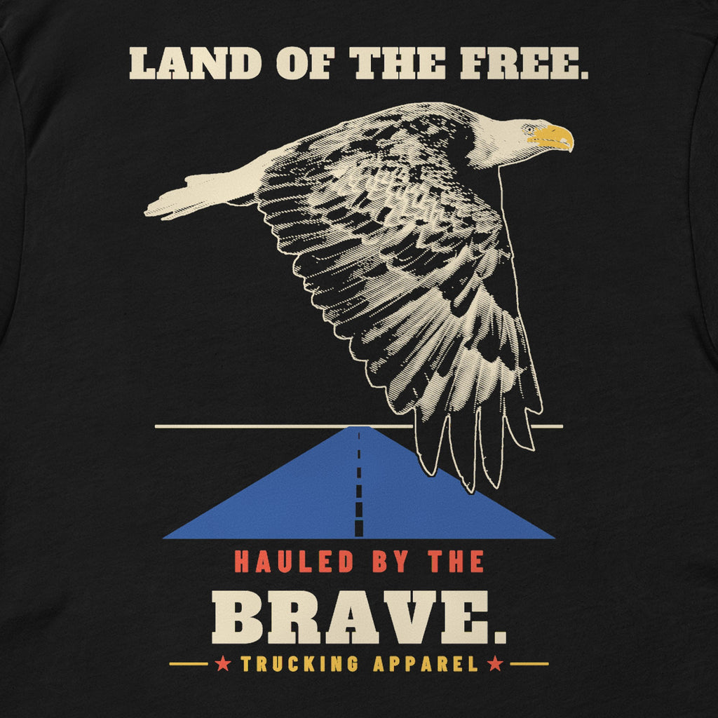 Land of the Free. Hauled by the Brave. Tee in black, close-up of the LAND OF THE FREE. HAULED BY THE BRAVE. back print: an engraving-style eagle over a highway.