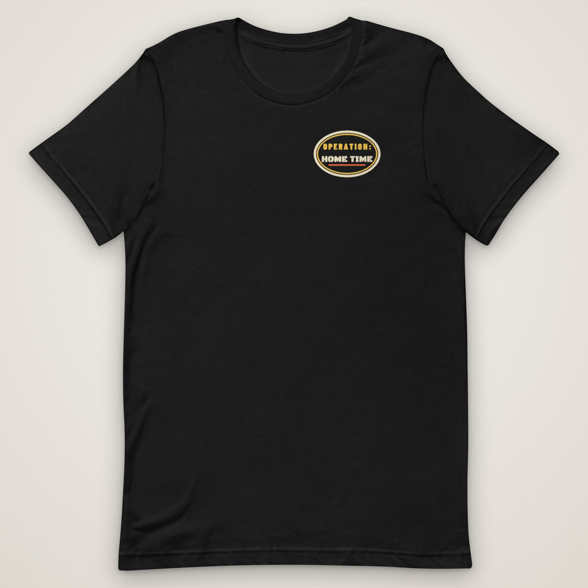 Operation: Home Time Tee in black, front view laid flat with the OPERATION: HOME TIME mission patch on the left chest.