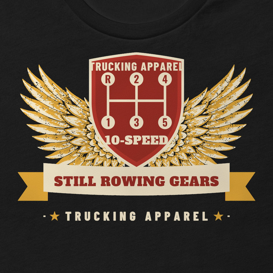 Still Rowing Gears 10-Speed Trucker Tee in black, close-up of the front print: STILL ROWING GEARS winged 10-speed shift pattern print. Design made with AI assistance.