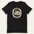 Big Rig Emblem Trucker Tee, front view laid flat showing a cream oval emblem with a big rig, crossed flags and three stars, with TRUCKING and APPAREL on solid bands.