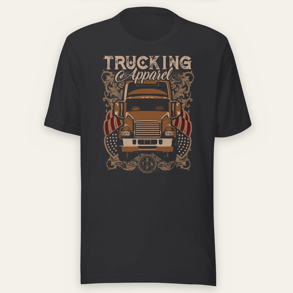 Trucking Cas Tee in black heather, front view laid flat showing an orange vintage big rig under a TRUCKING Apparel script headline with ornate scrollwork and American flag accents.